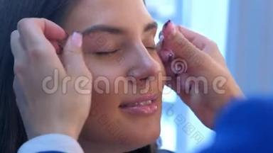 化妆师在沙龙中将基色调霜涂在女孩眼皮上摩擦手指。